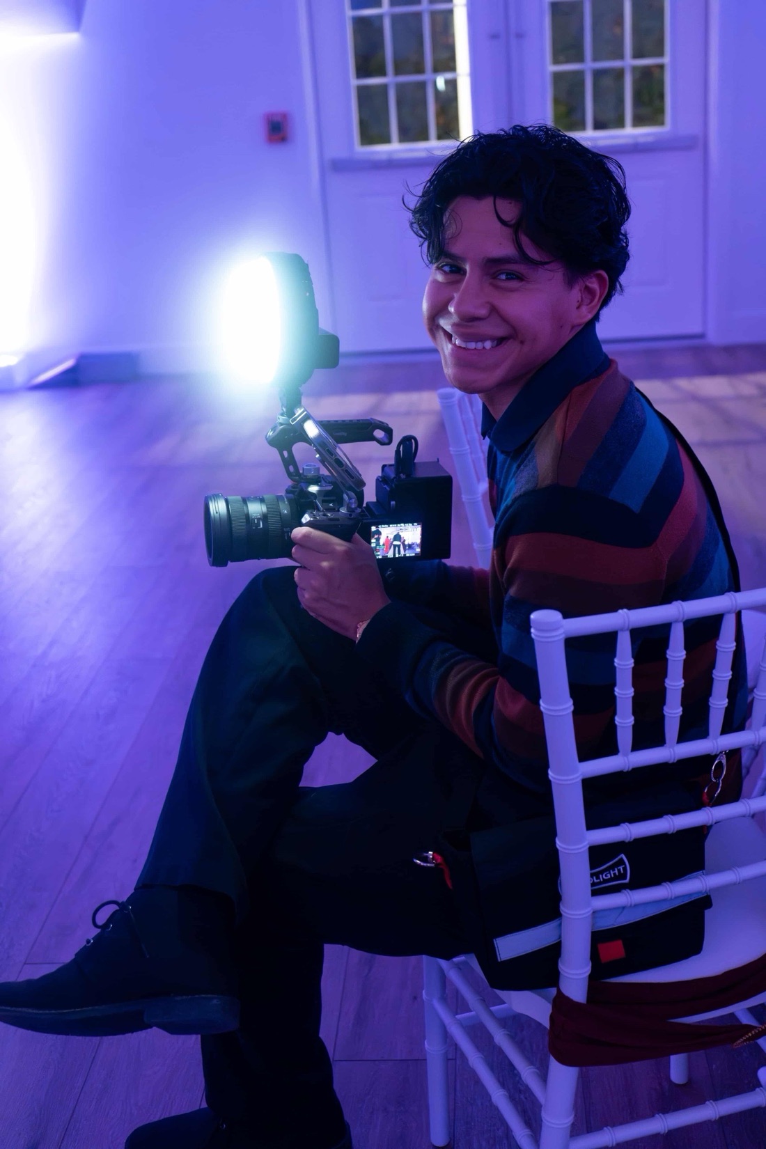 Deivin turning back mid-shoot with his camera rig, grinning, in a purple-lit event hall